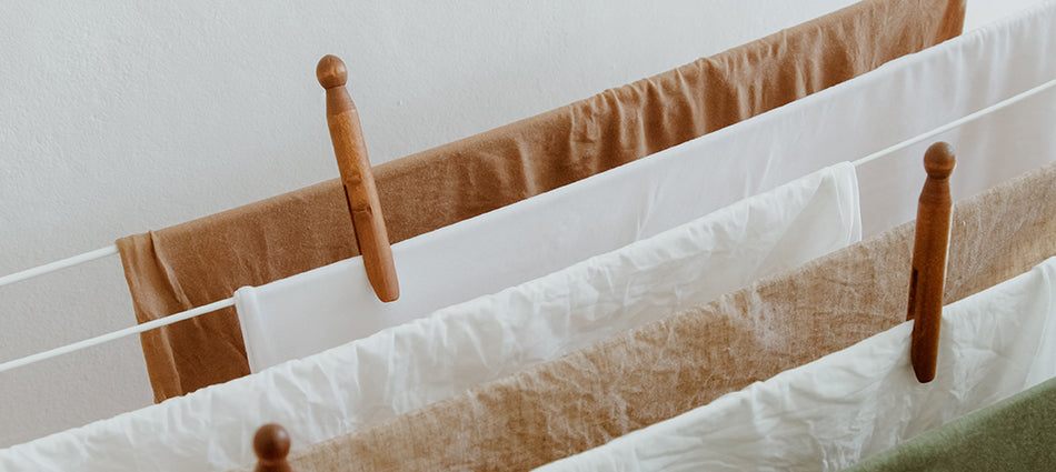 Several natural-looking fabrics are draped over a clothesline and are held in place by vintage wooden clothespins.