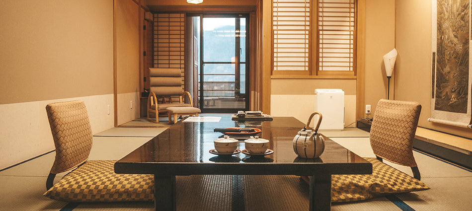 A low table and two chairs sit in the middle of a modern Japanese-style living room.  The floor is covered with tatami mats.  The table is set for tea.