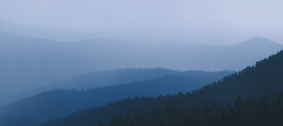 The Great Smoky Mountains are shown in panorama shrouded in mist.  It is twilight, and each ridge appears to be a different shade of blue.