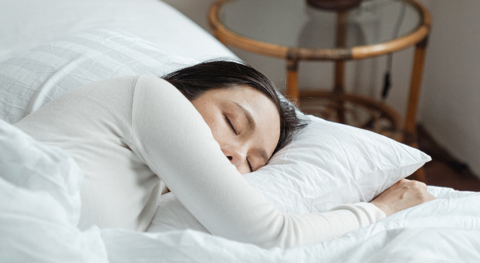 A woman is sleeping on a mattress. The bed is made with all white bedding.