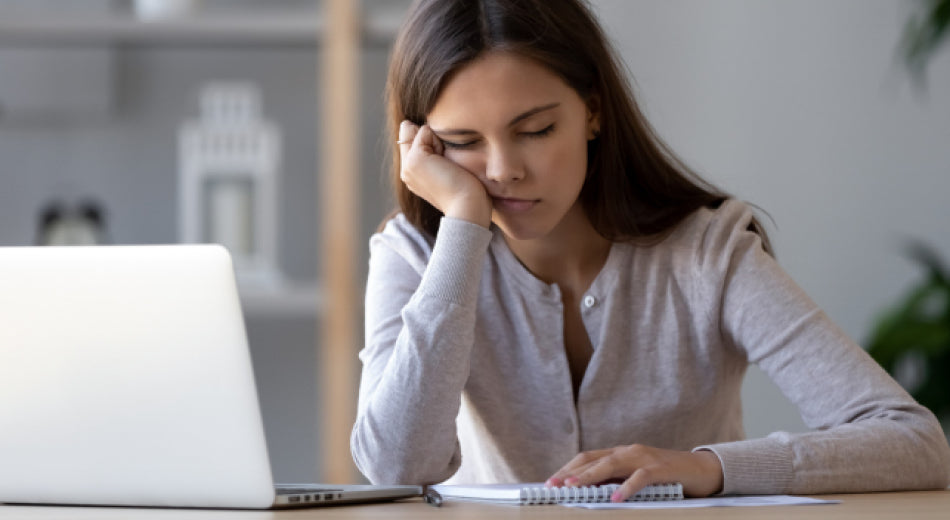 A woman is sitting at a desk with her eyes closed. 