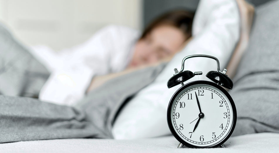 An alarm clock with a woman sleeping next to it.