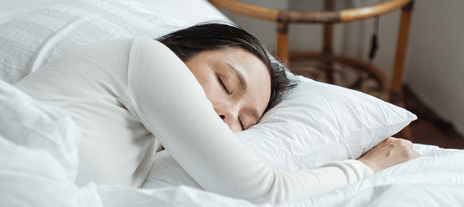 A woman naps on a bed dressed in white sheets.  She is laying on her side.  It is daytime and the room is filled with light.