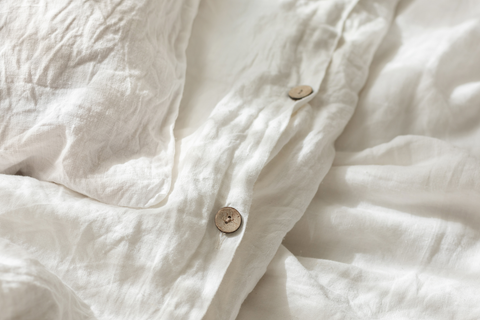 Close-up on the faux coconut buttons at the bottom of a white duvet cover. Parts of the duvet and matching pillow sham are shown. They are rumpled for a “lived-in” look