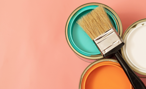 A paintbrush sits on top of three open cans of paint – white, orange, and teal.  The background is a coral color.