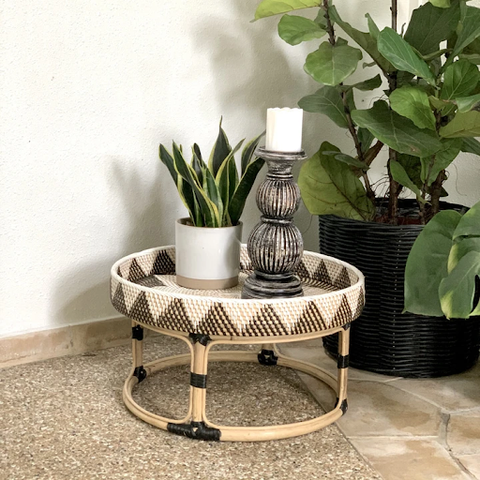 A side view of the Nana Round Table with a potted plant and candle holder on top