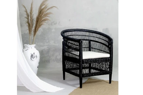 A black rattan chair with a white cushioned seat placed beside a white vase