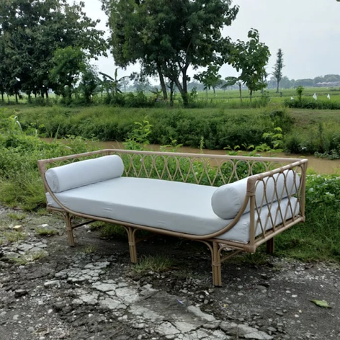 A wide natural rattan chair with a white cushion seat and two bolster cushions placed outside