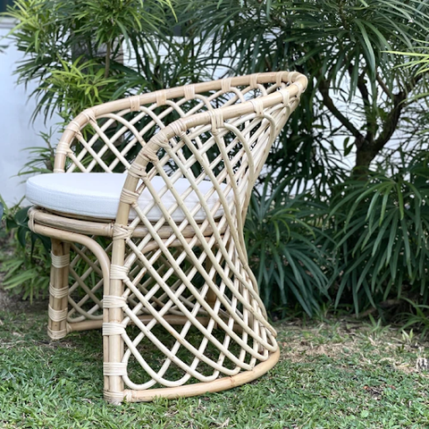 A natural rattan chair with a white cushioned seat in a garden