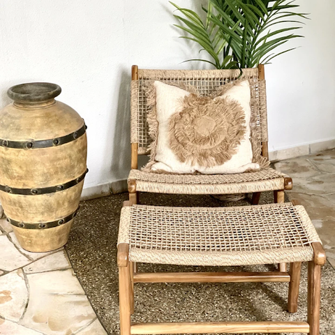  A natural rattan chair with a white pillow and footrest is placed beside a wooden vase