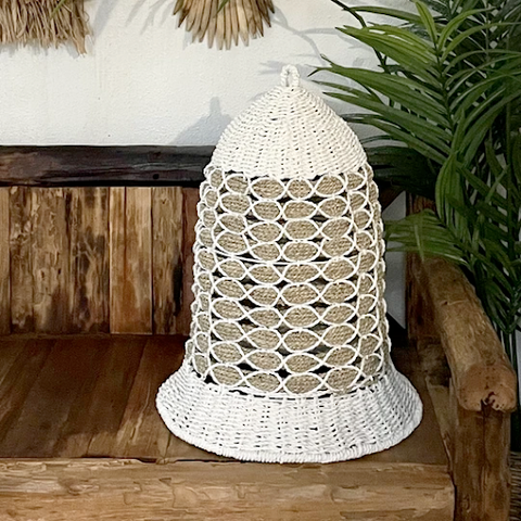 An egg-shaped rattan lamp with white accents on a wooden bench