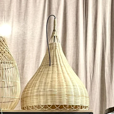 A cone shaped rattan lamp in front of a beige-colored curtain