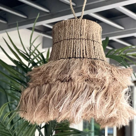A fringed rattan lamp hanging above outdoor plants