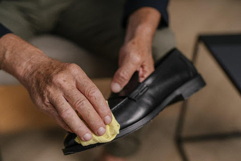 A person cleaning a black leather shoe