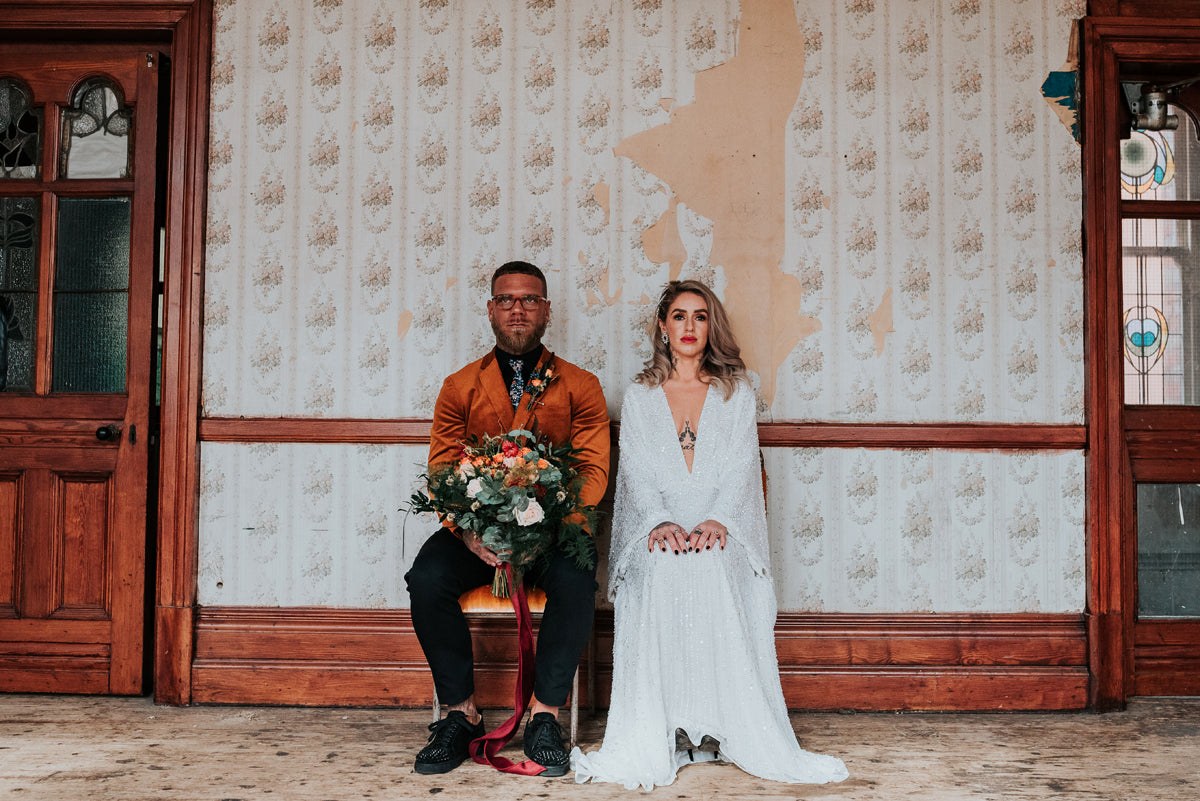 Bride and groom sat waiting outside room holding flowers