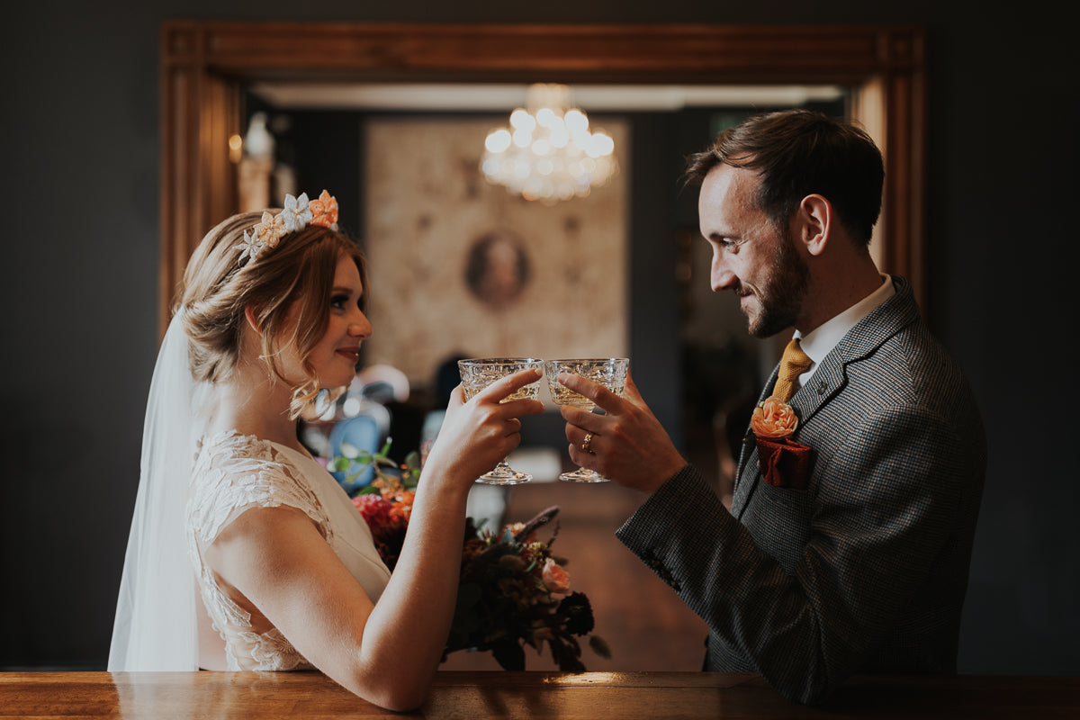 Bride and groom clinking glasses with groom wearing yellow gold plain wedding band