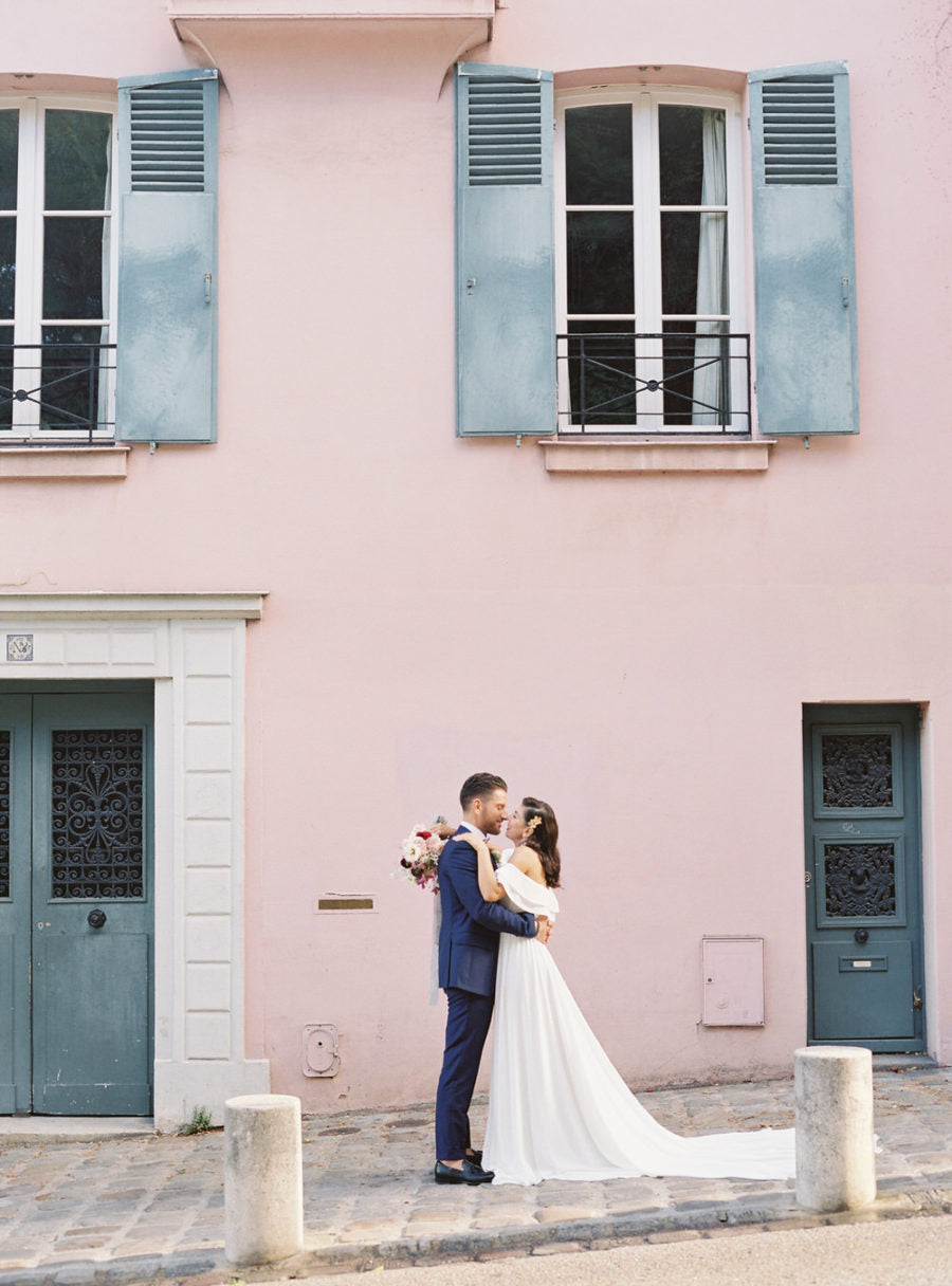 Bride and groom embrace outside pink building with blue doors