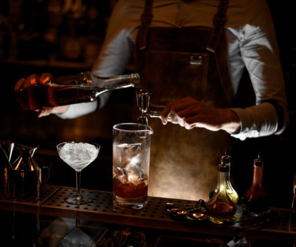 Bartender pouring liquor in a jigger under dim lighting