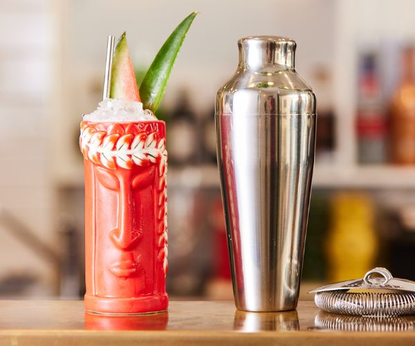Cocktail in a unique human-face designed glass with cocktail M Shaker and strainer