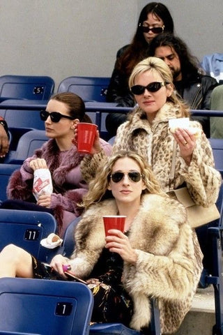 Image from the series Sex & The City of characters Samantha, Charlotte and Carrie sitting at a game holding red cups