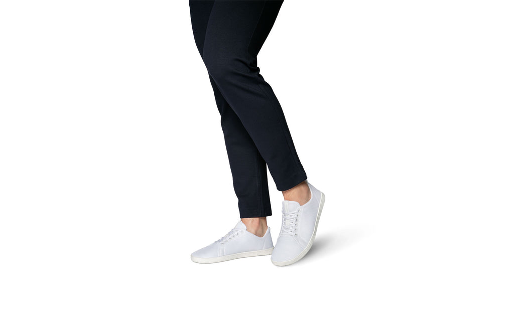 Model trägt weiße Barfußschuhe des Modells Original Mesh der Marke Feelgrounds zu dunkelblauer Hose