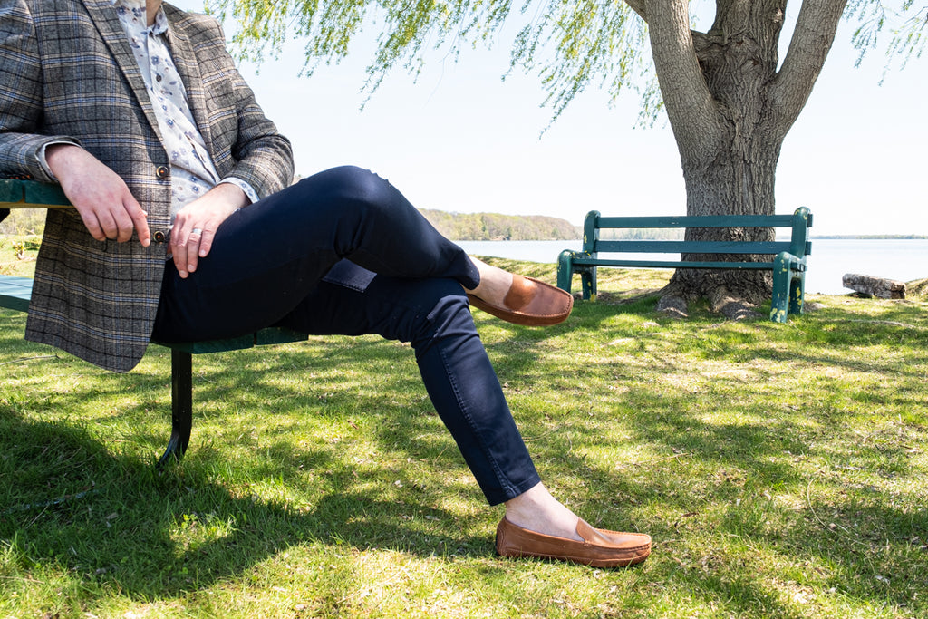 Man sitting on a park bench dressed in business casual with a pair of brown slip on loafers