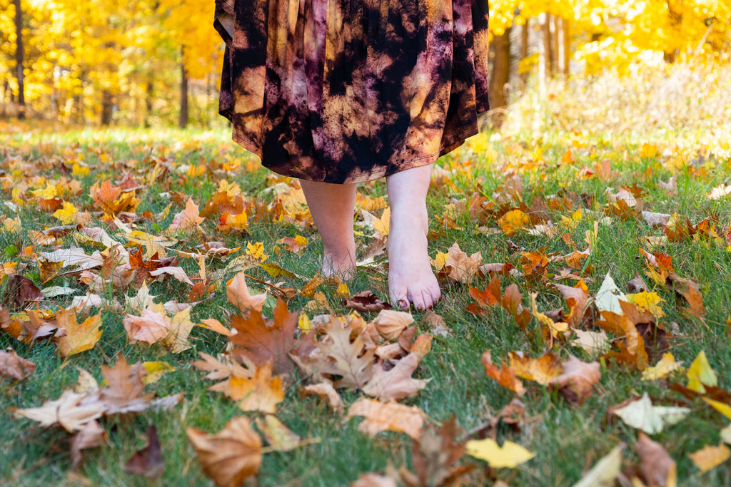 Women walking barefoot in the grass in the fall with colorful leaves on ground