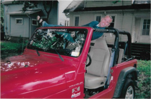 Man relaxing in hammock mounted over the front seat of his red Jeep Wrangler 