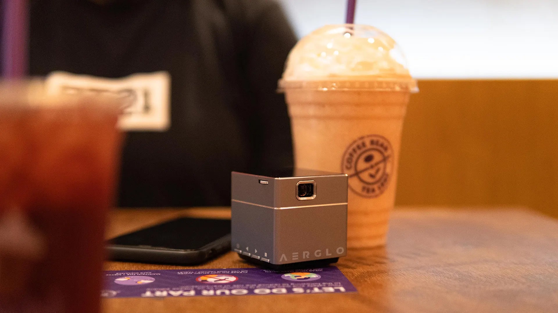 Aerglo Neutrino Smart Mini Projector - at a drink cafe round table with smoothie drink