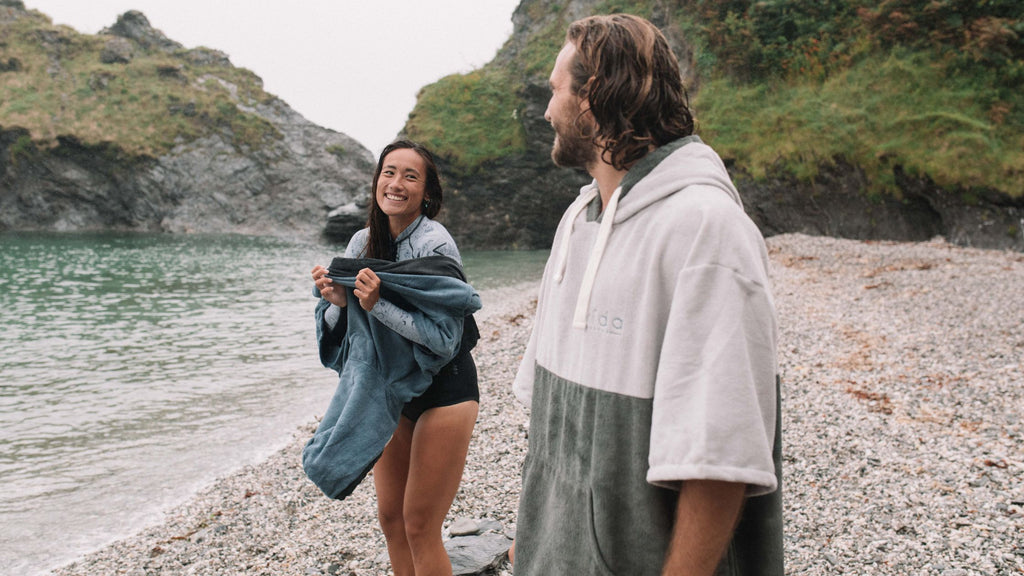 A man and a woman changing on a beach with poncho towels