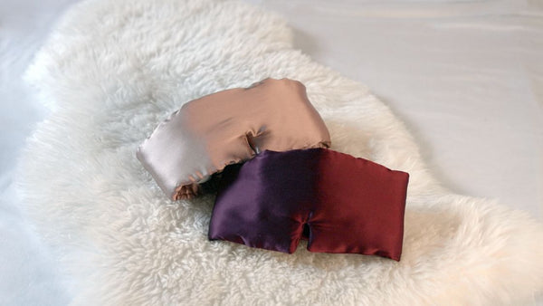 Two silk sleep eye masks lying on a fluffy blanket on a bed