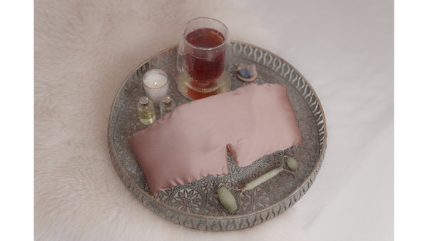 A tray of items for a bedtime ritual - herbal tea, silk eye mask, face roller, crystals - Vivida Lifestyle