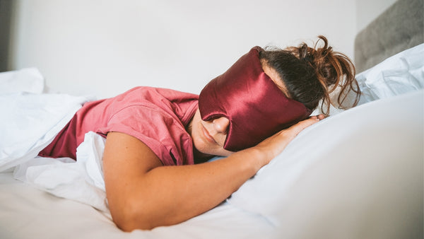 Woman sleeping in a bed wearing a silk sleep mask - Vivida Lifestyle