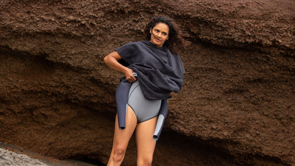 Woman changing into a wetsuit under a poncho towel