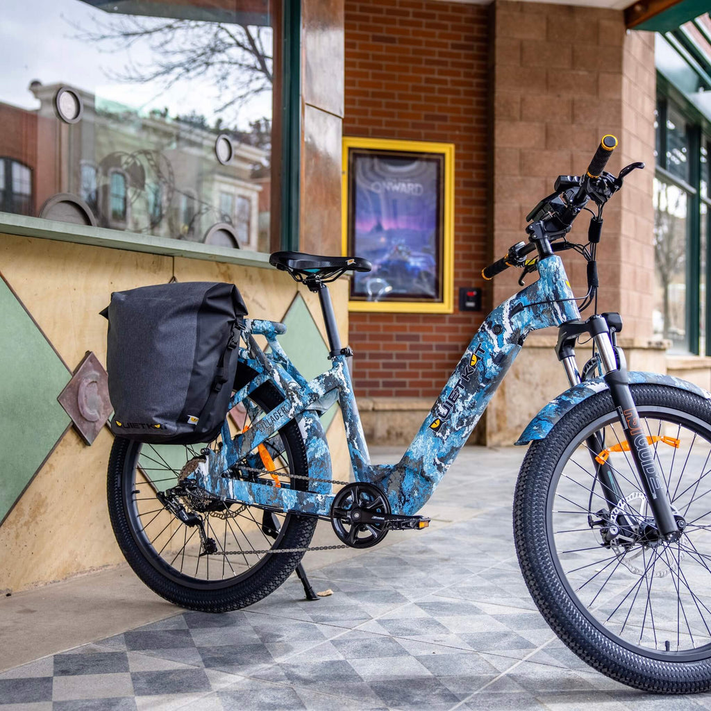 Un vélo électrique QuietKat Villager avec sacoches est garé devant un café.