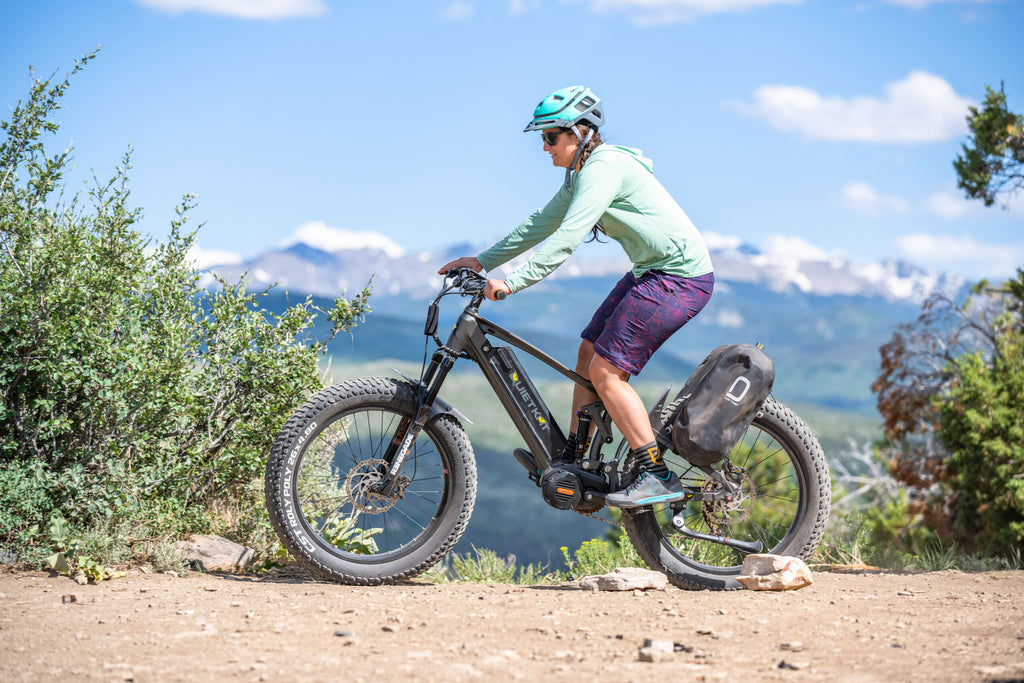 Une femme pilote son vélo électrique avec des accessoires, comme des sacoches, le long d'un chemin de terre.