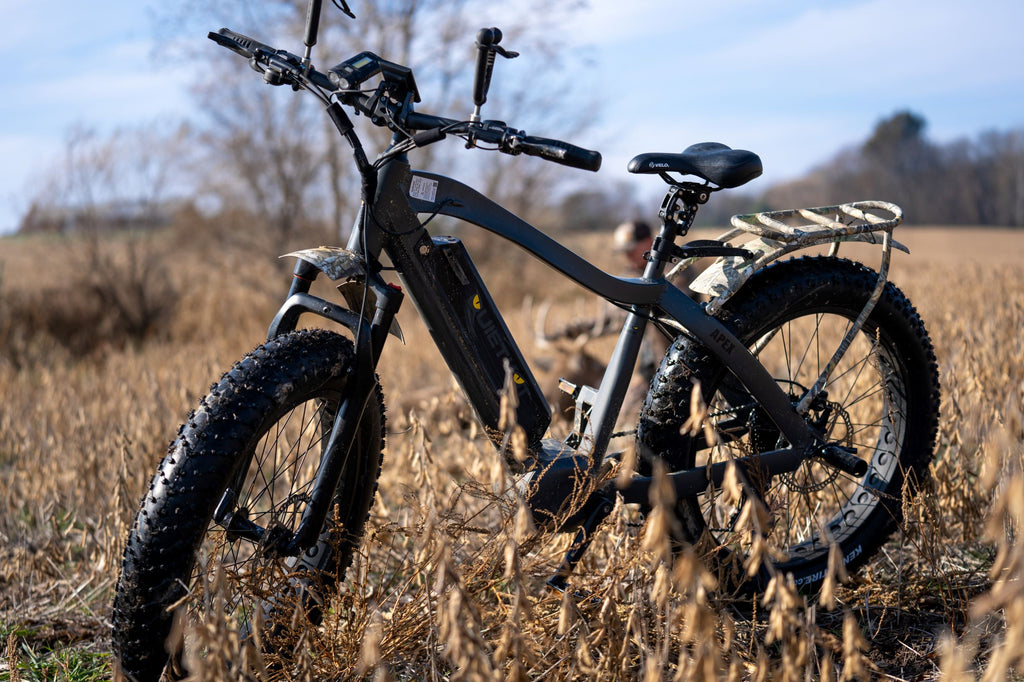 Un vélo de chasse électrique QuietKat Apex se dresse dans un champ herbeux