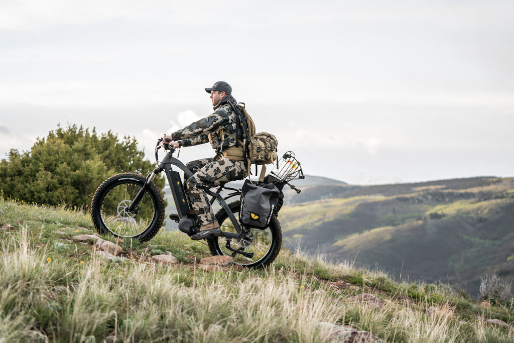 A hunter wearing camo climbs a steep hill on his QuietKat electric hunting bike
