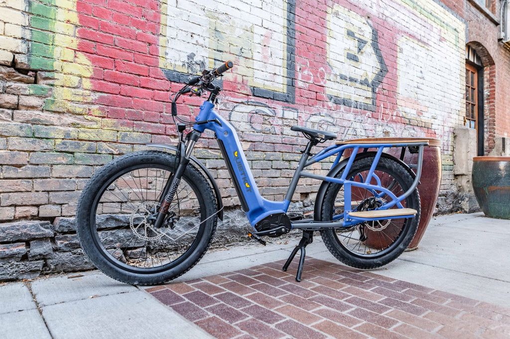 Profil d'un vélo électrique bleu près d'un mur de briques avec des graffitis.