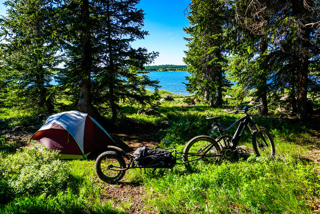 Un vélo électrique QuietKat se trouve près d'une tente au bord d'un lac