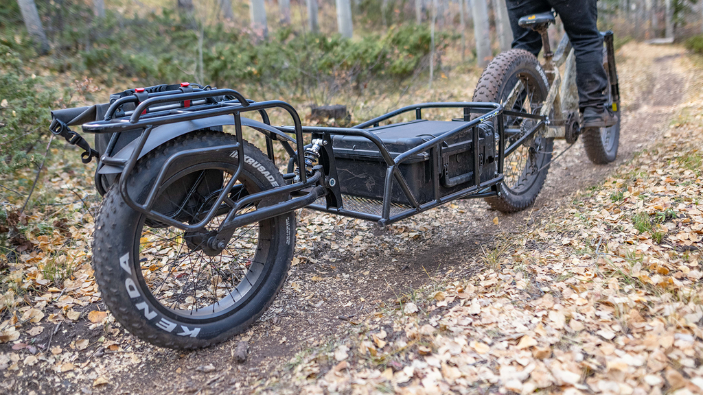 Un vélo électrique QuietKat tire une remorque à une roue à travers les bois.