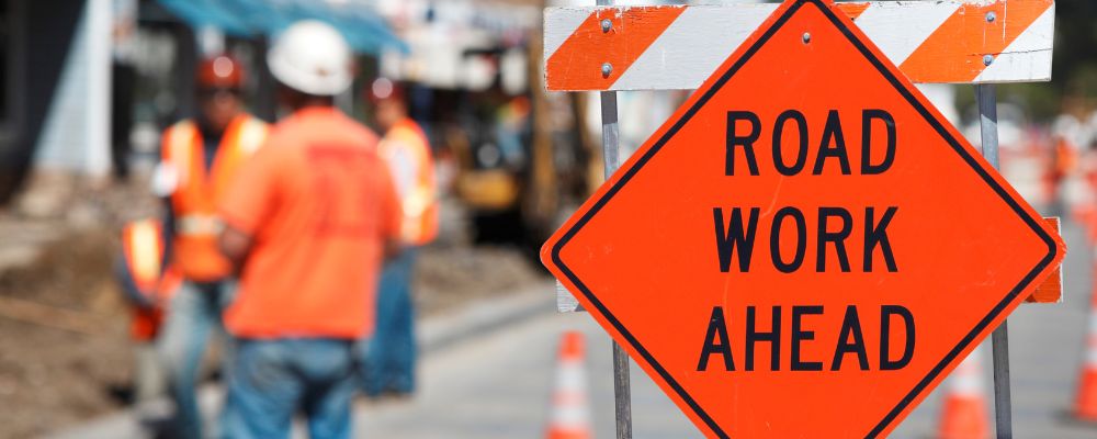 road work ahead sign with workers wearing safety vests