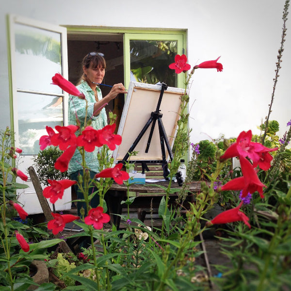 Artist Joanne Short at work painting in her garden painting using an easel and canvas.