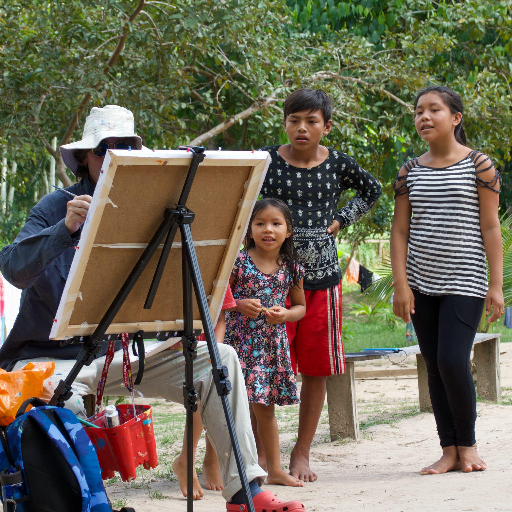 A young Amazon Indian family watch as John Dyer paints the tribal village in the rainforest of Brazil