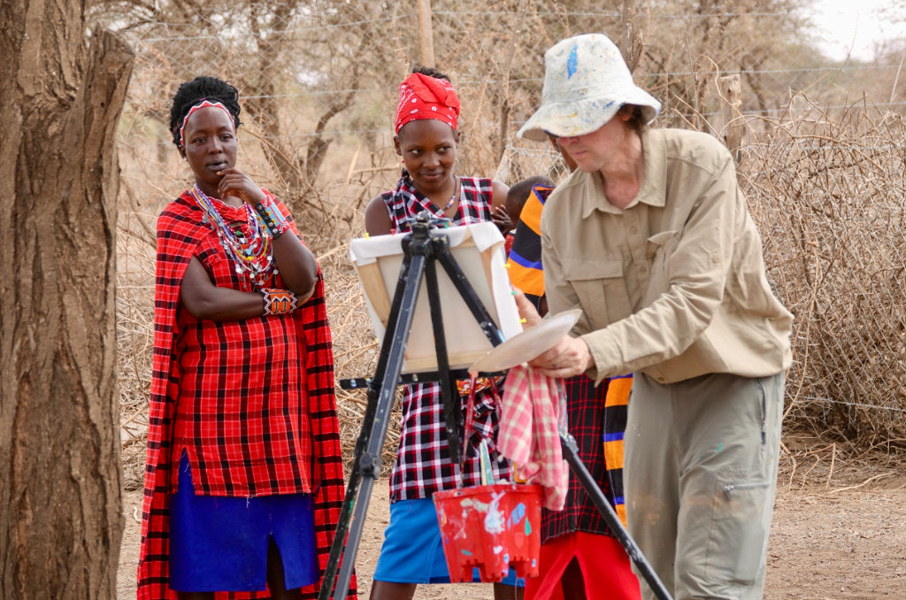 John Dyer pictured painting Maasai women in a traditional boma setting in Kenya, Afrcia