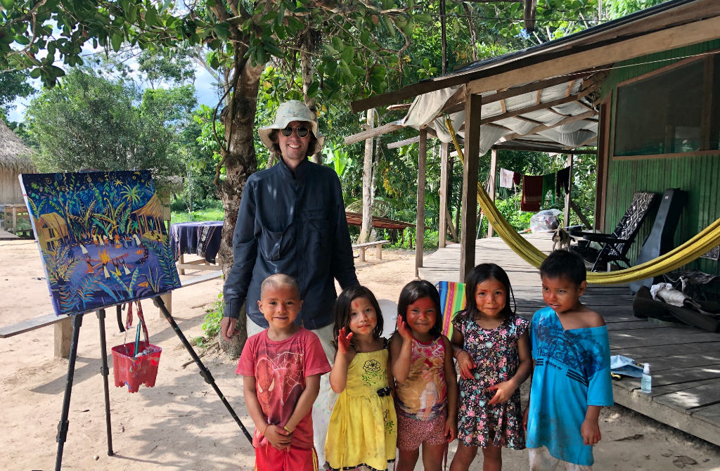 John Dyer surrounded by Amazon Indian children as he paints in the tribal village of Mutum in the Amazon Rainforest in June 2019