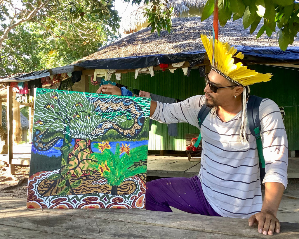 Nixiwaka Yawanawá holding a painting in the Amazon rainforest