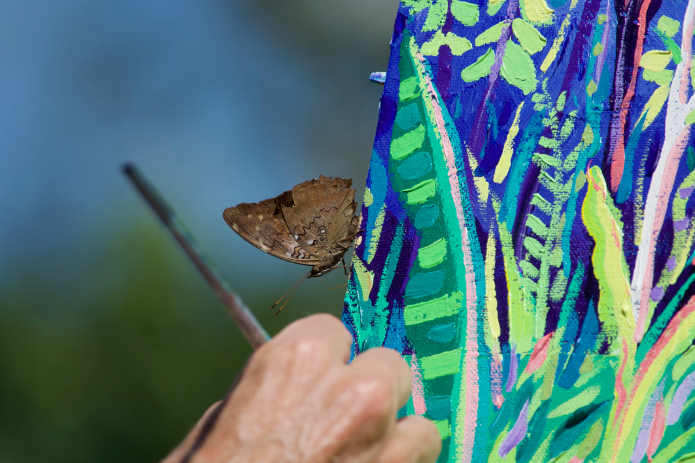 An Amazon rainforest butterfly rests on the edge of John Dyer's painting as he paints deep in the jungle