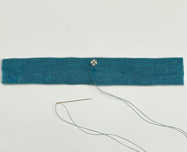 A blue strap with the ball end of the snap set sewn on one side, and a needle and thread inserted 3/8" from the centerline on the other side.