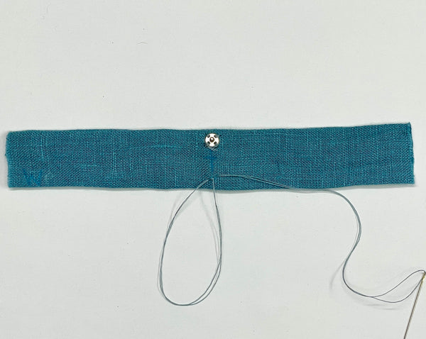 A blue strap with the ball end of a snap set sewn on one side, and a needle and thread creating a loop on the other side.